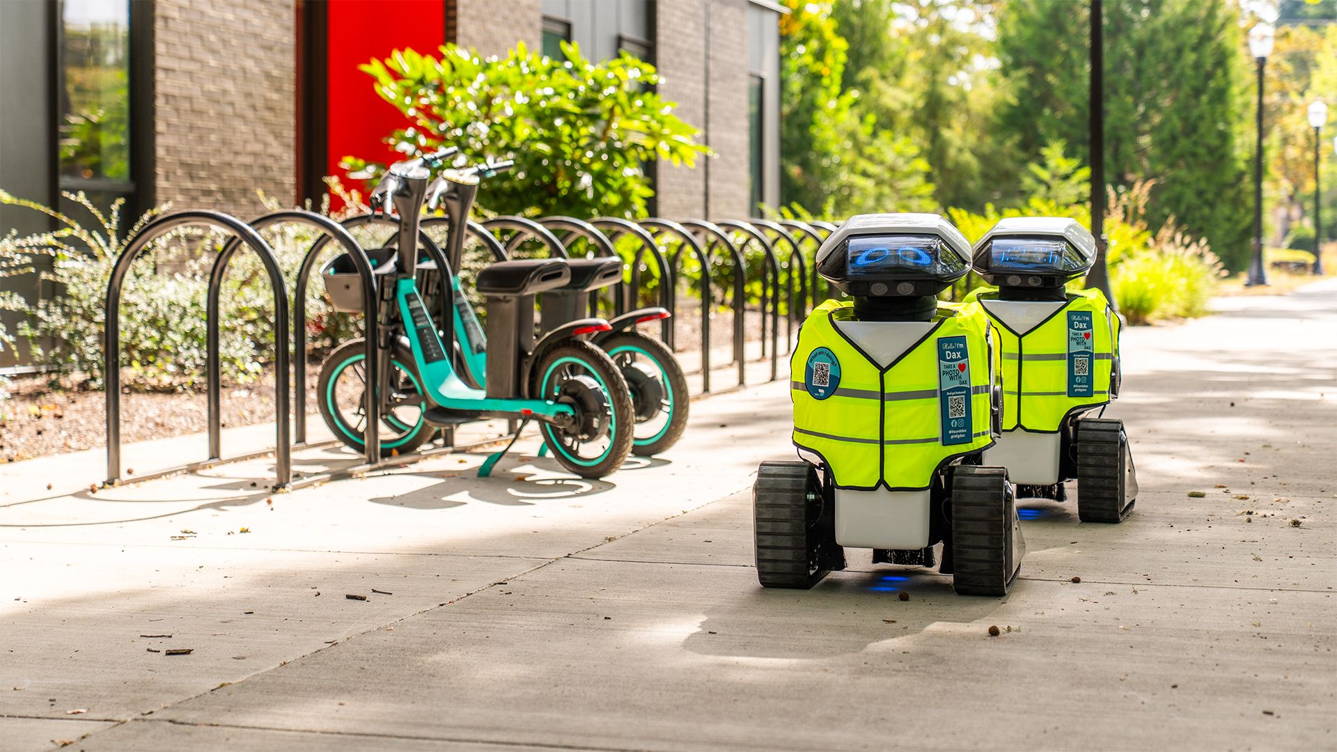 Two Dax robots in hi-vis vests assessing a sidewalk