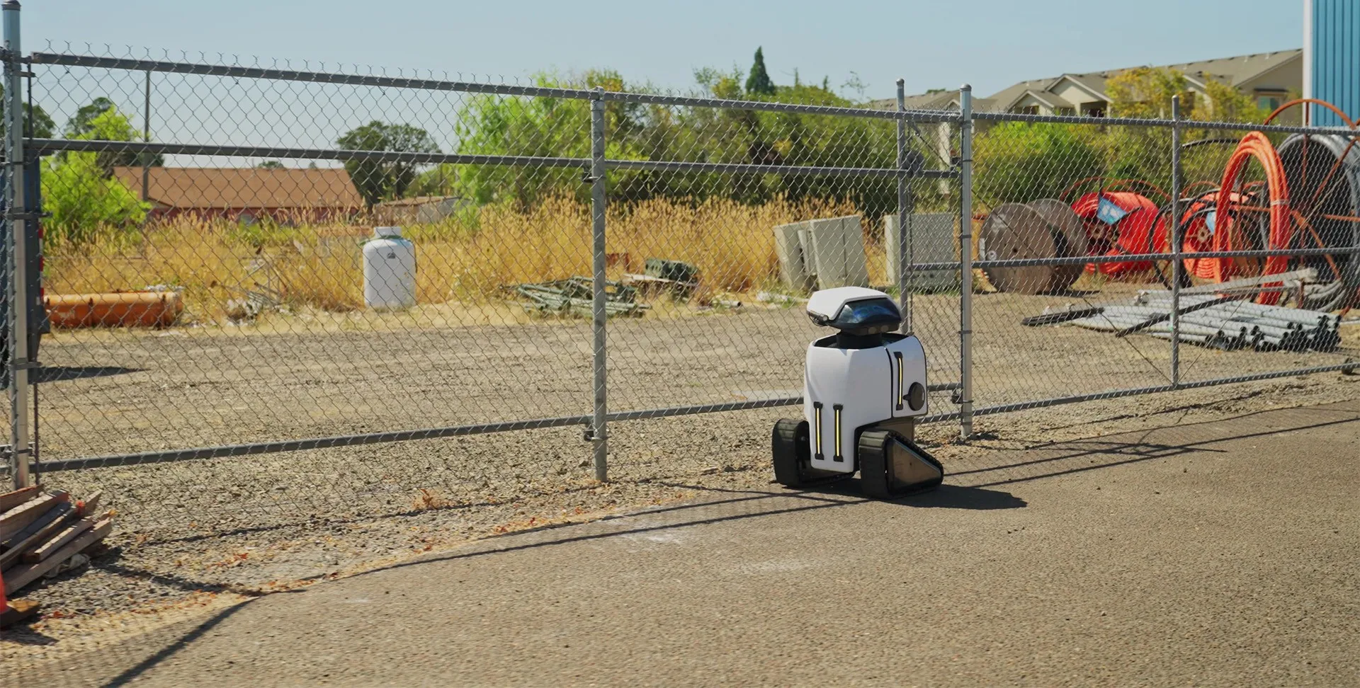 A Dax security robot on patrol beside a fenced commercial lot