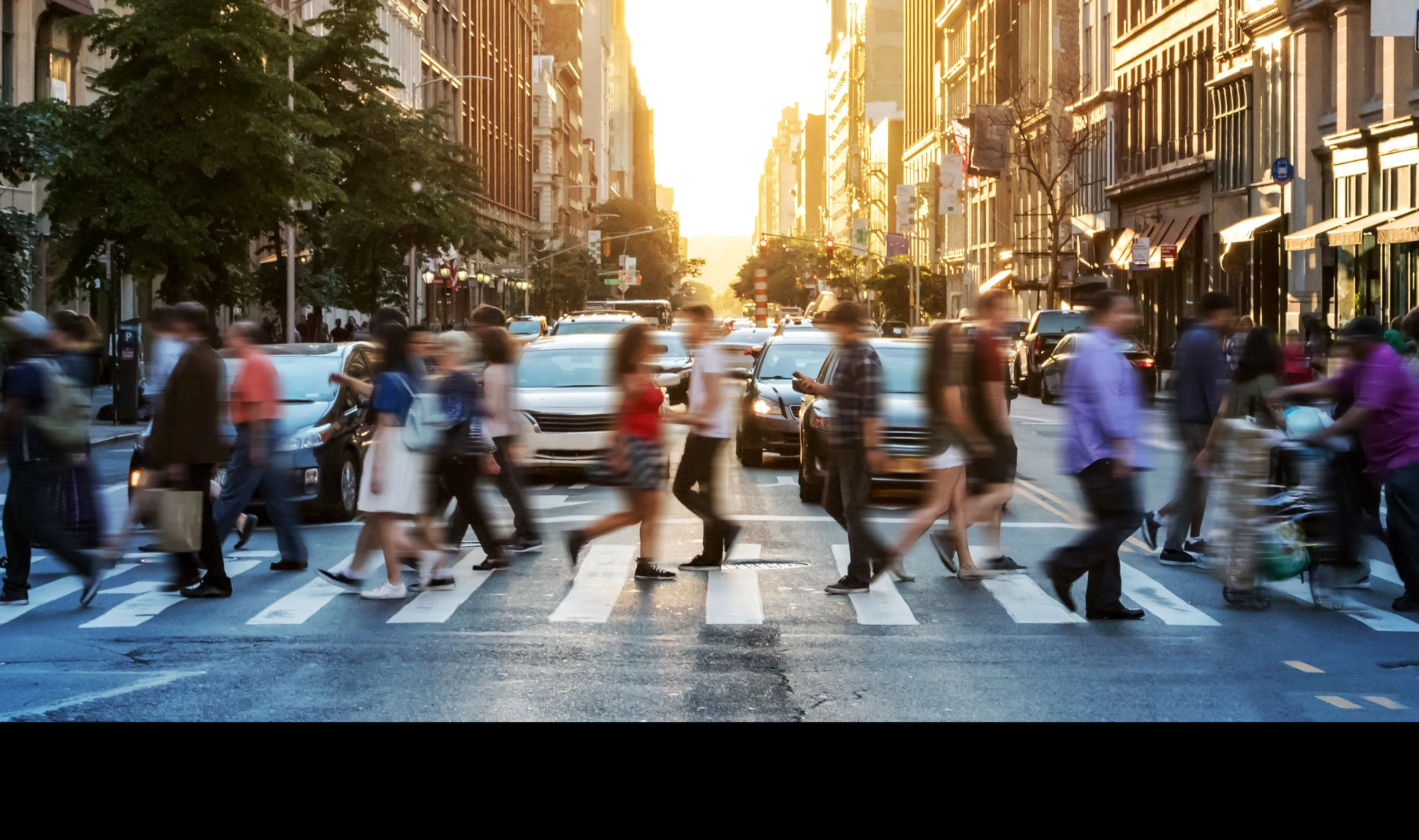 Pedestrians crossing a busy city street at sunset
