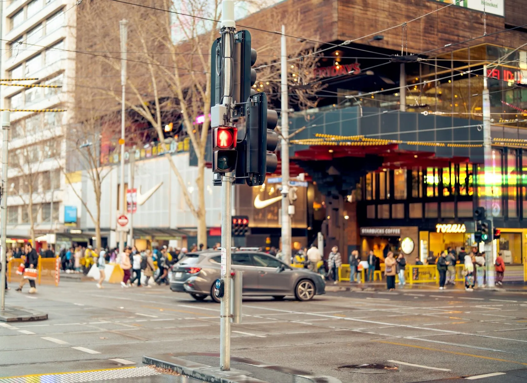 A busy downtown crosswalk with a pedestrian signal and curb ramps