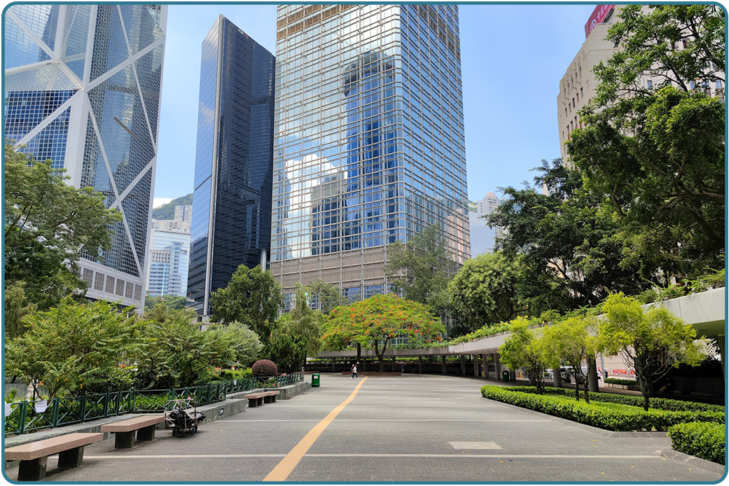A public plaza with trees and benches between downtown office towers