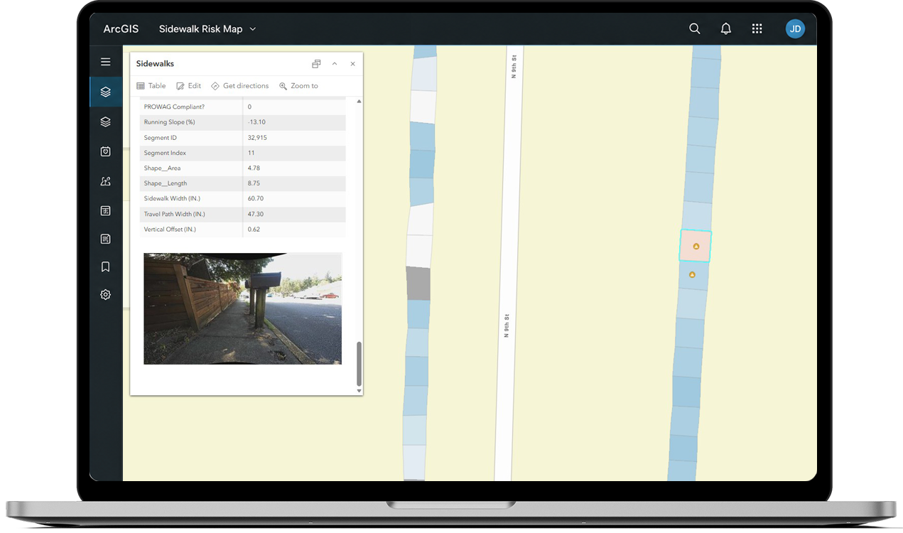 An ArcGIS segment report on a laptop: PROWAG compliance fields, measurements and a site photo for a selected sidewalk segment