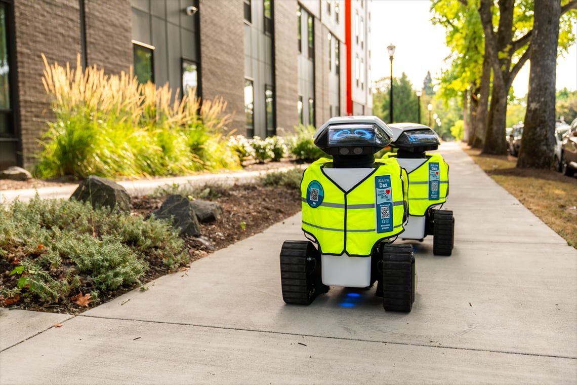 two Dax robots roll along a sidewalk